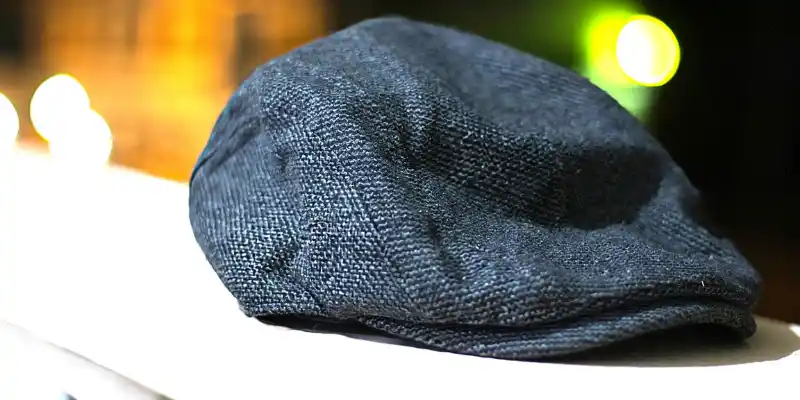 A dark flat cap placed on a white railing with blurred lights in the background at night