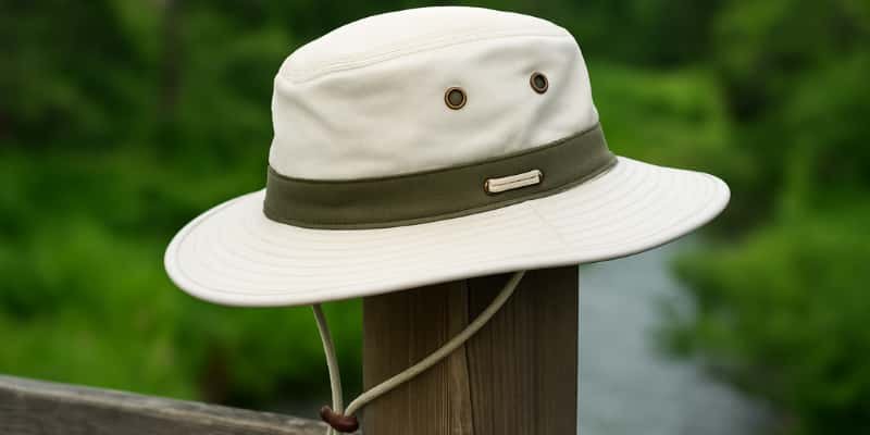 A classic off-white Tilley hat with a chin strap resting on a wooden post in a natural outdoor setting