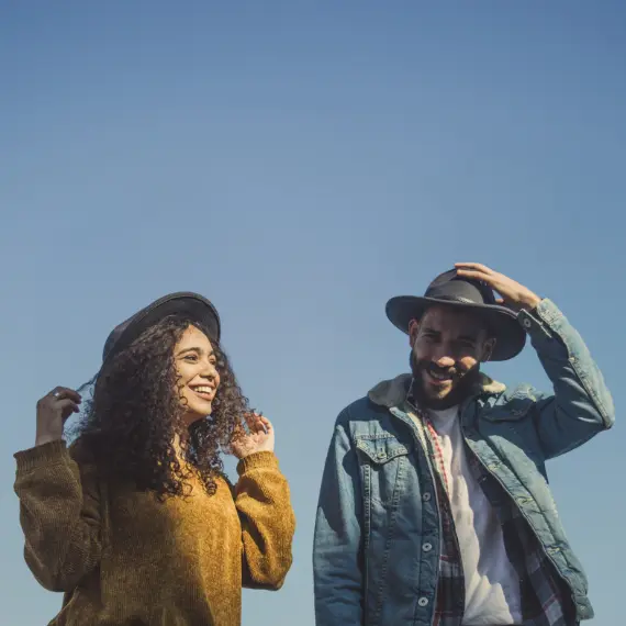 Home 1 A smiling man and woman wearing fashionable hats, with the man adjusting his hat