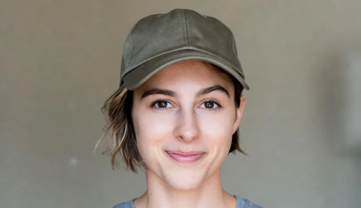 Woman with short hair wearing a baseball cap with one side tucked behind the ear
