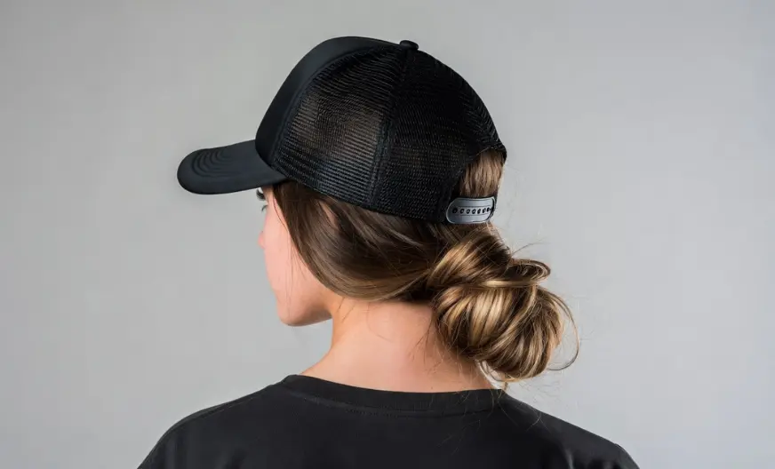 How to Wear a Hat with Long Hair Without Ruining Your Style 15 Back view of a woman with long hair wearing a black trucker hat with a mesh back and a messy low bun hairstyle