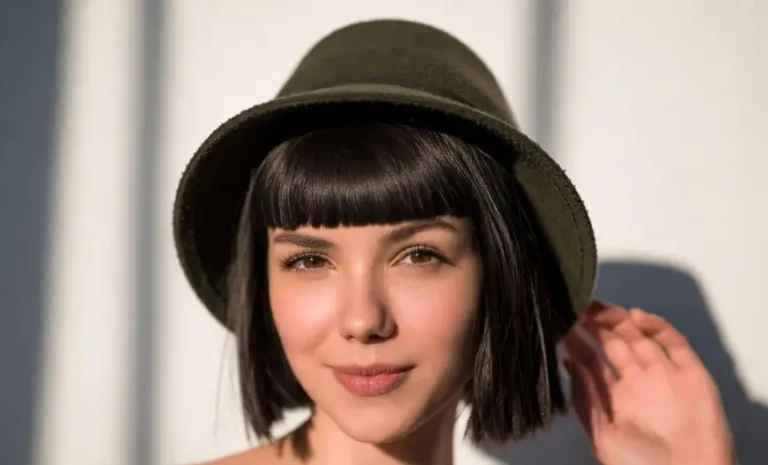 A woman demonstrating how to wear a hat with short hair featuring a dark green wool cloche hat over a brunette bob with blunt bangs.