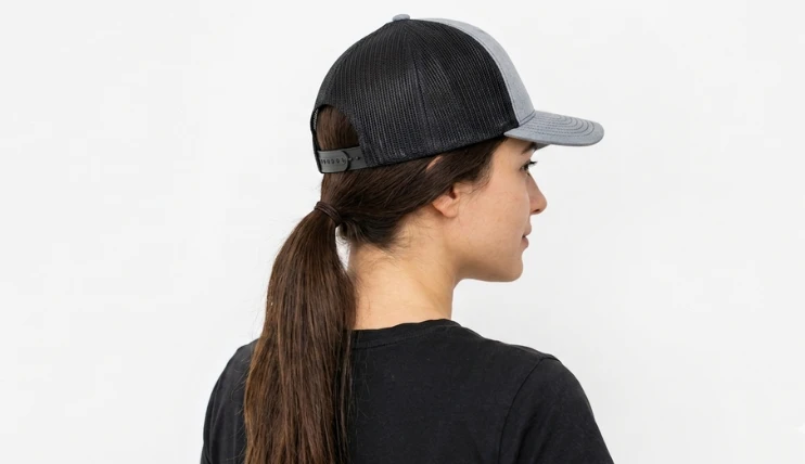 Woman wearing a trucker hat with long hair in a low ponytail