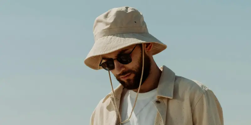 26 Different Types of Hats Explained (With Names, Styles & Pictures) 10 Beige bucket hat with chin strap worn by a man in casual summer outfit outdoors
