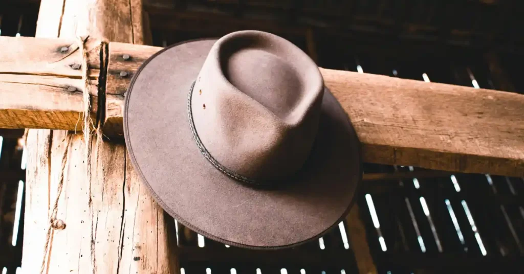 Brown felt cowboy hat hanging on a rustic wooden barn beam with natural light filtering through the background