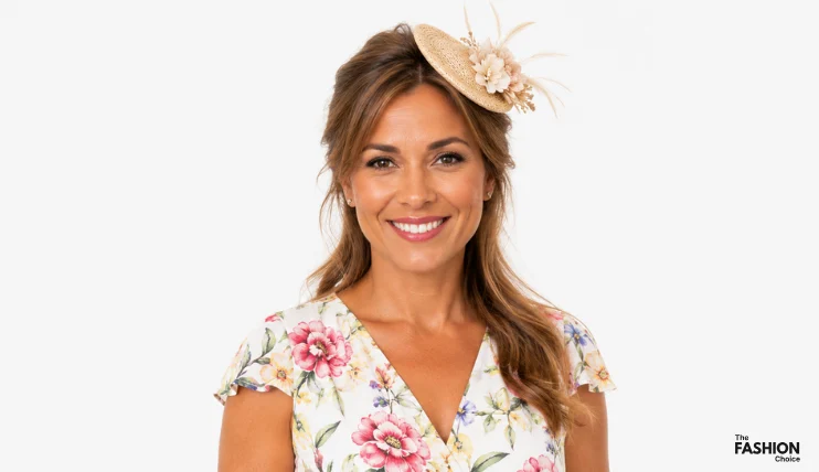 Woman with loose wavy hair wearing a small natural straw fascinator with flowers and feathers, styled with a floral summer dress for a garden party or outdoor event