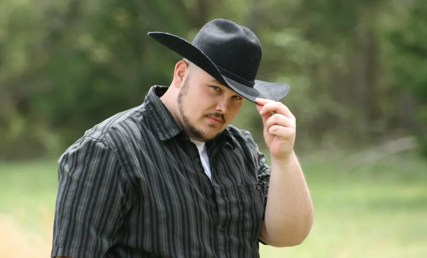 Man wearing a black cowboy hat, demonstrating how to wear a cowboy hat correctly in a natural outdoor setting.