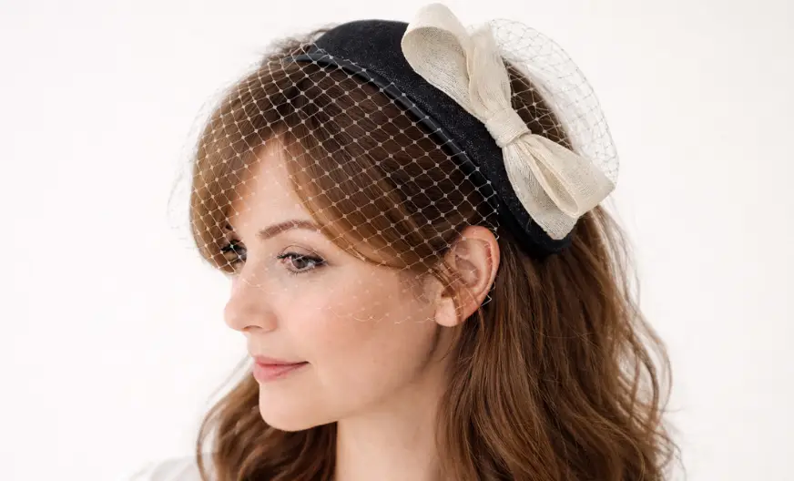 Adult woman wearing a fascinator with netting placed correctly over the forehead, showing secure headband support and natural textured hair