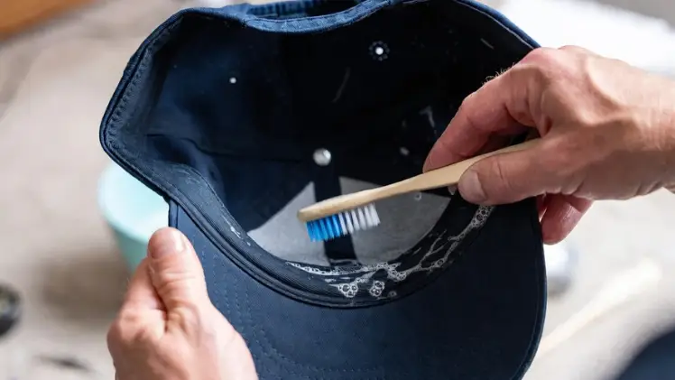 How to Deodorize a Hat: 5 Simple Ways to Kill the Stink Without Ruining It 7 Using an old toothbrush and mild dish soap to scrub the inner sweatband of a navy blue cap in small circular motions.