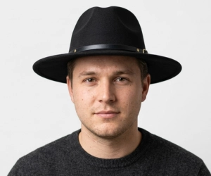 man with a round face wearing a wide brim fedora hat