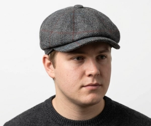Man with a round face wearing a herringbone tweed newsboy flat cap.