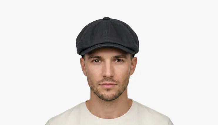 A man with a heart-shaped face wearing a dark grey newsboy cap.