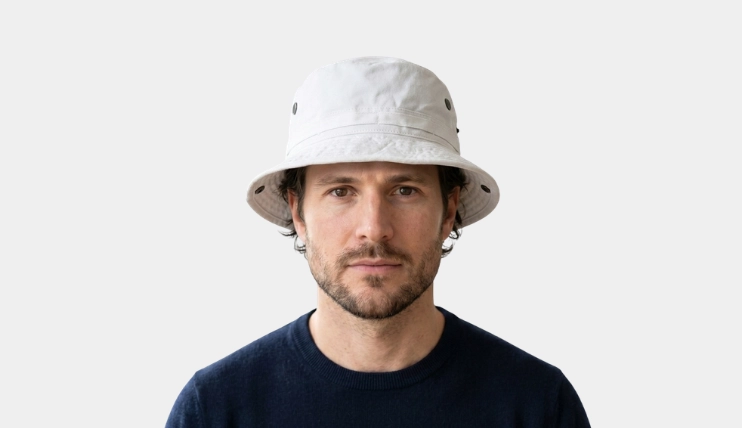 Man with square face wearing a white boonie hat on a plain background