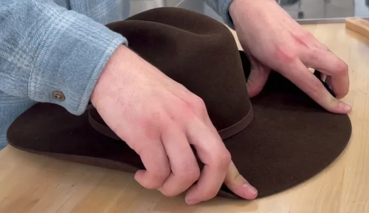 Hands pulling up both sides of a felt cowboy hat brim