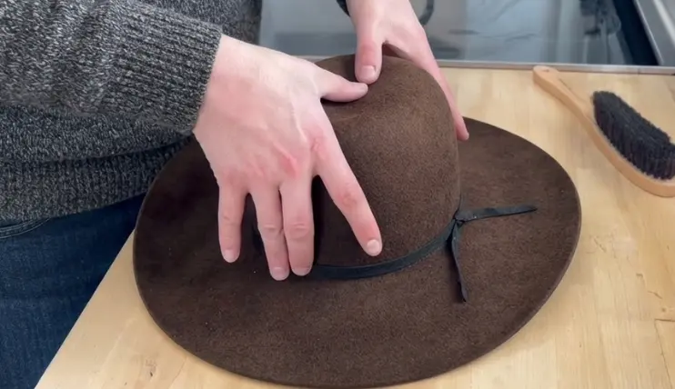 Hands shaping a shallow center crease in a felt cowboy hat