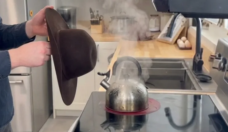 Man steaming a felt cowboy hat over a tea kettle before shaping it
